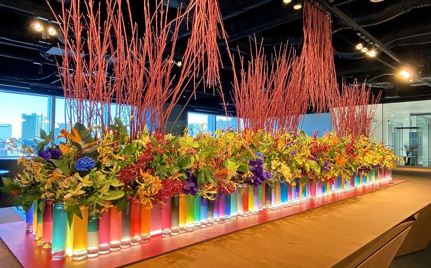 色とりどりのガラスの花器を並べ、赤い枝を高く挿した企業の受付の迎春装花