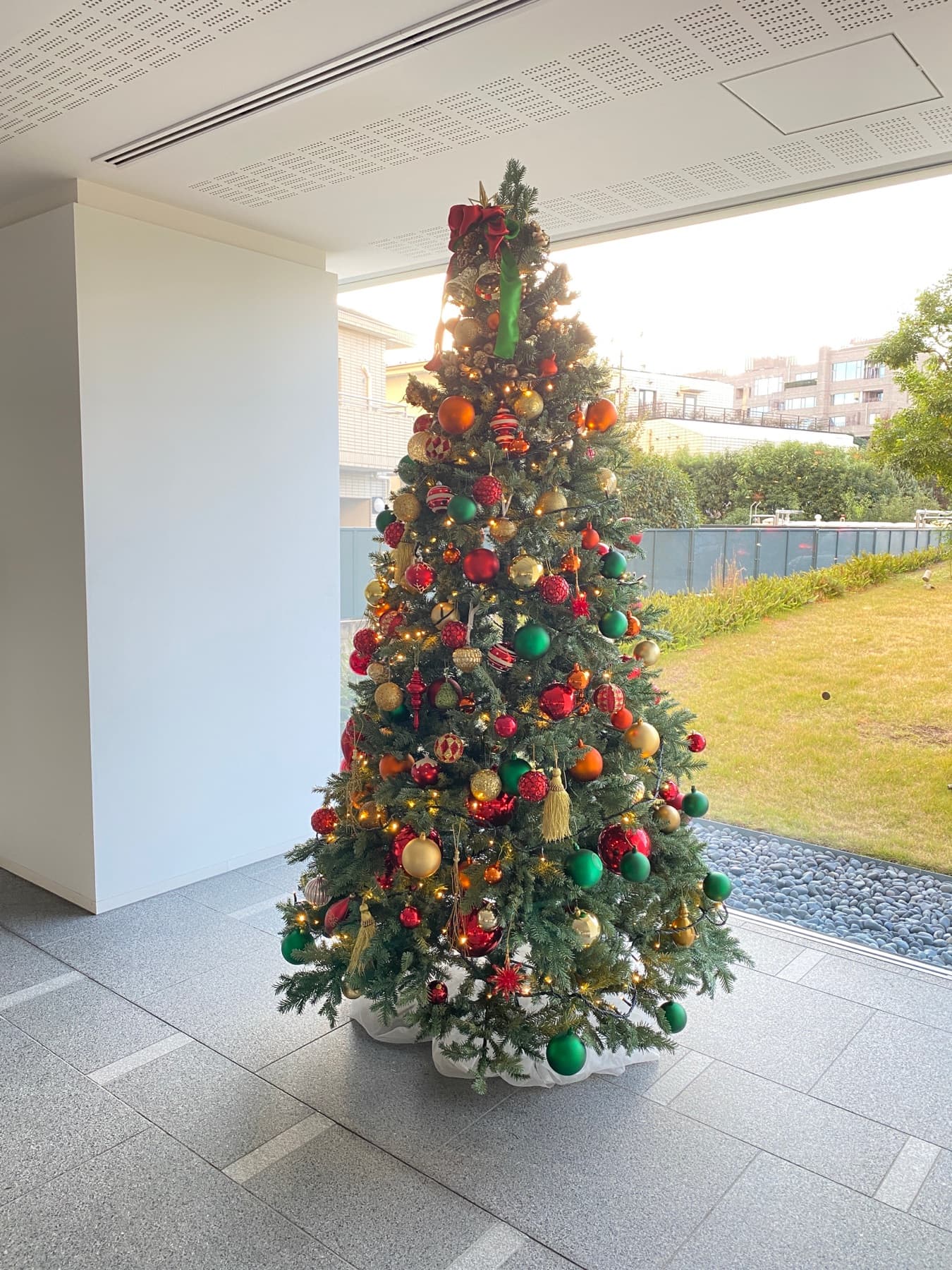 ガラス越しに庭が見えるエントランスに置いた、赤・金・緑のオーナメントのクリスマスツリー